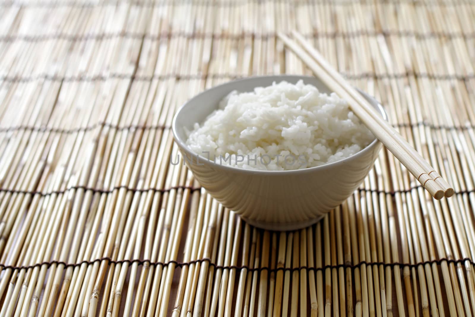 A bowl of rice and chopsticks on bamboo