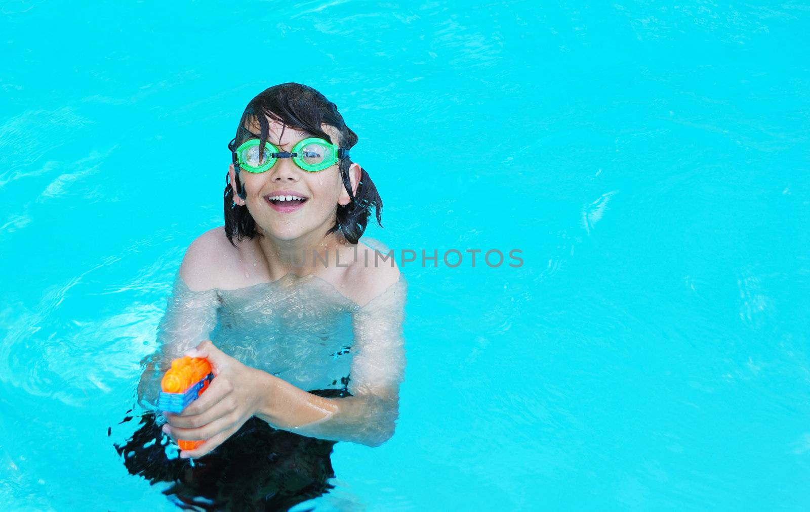 Smiling teenage boy in the pool pointing an orange water gun.