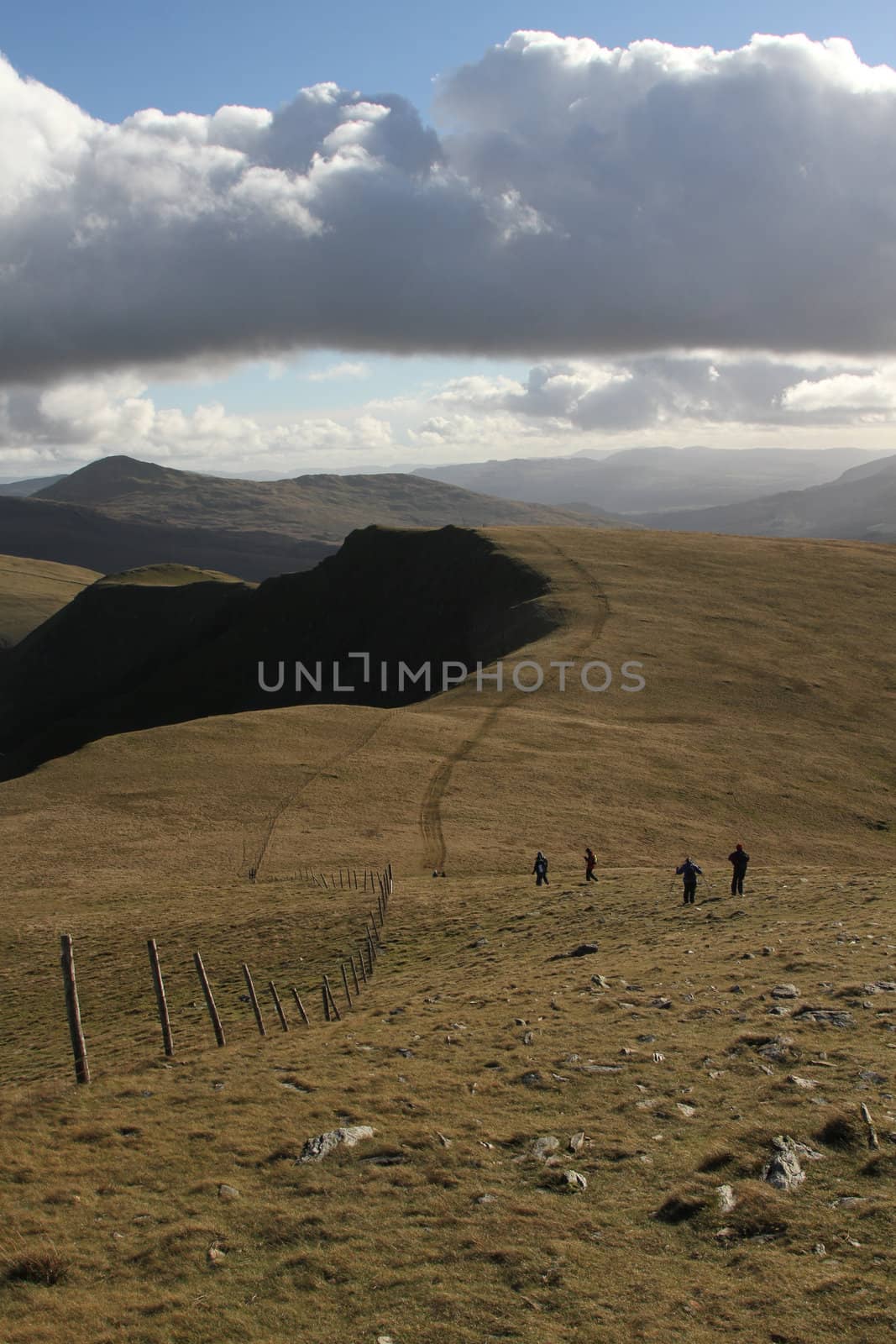 Hill walkers enjoying the great outdoors on a grassy mountainside  with blue sky and cloud.