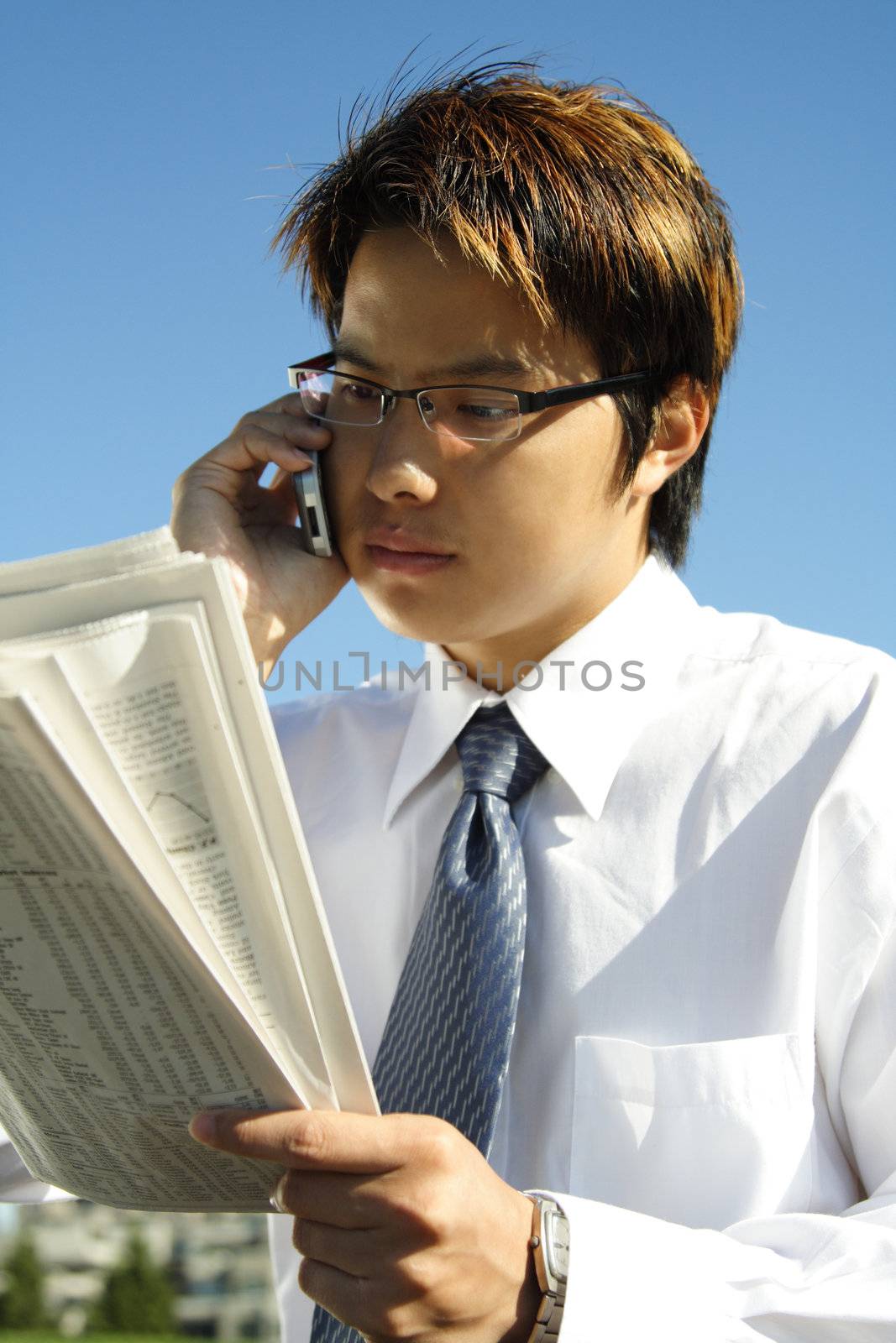 Businessman reading a financial newspaper while making a phone call