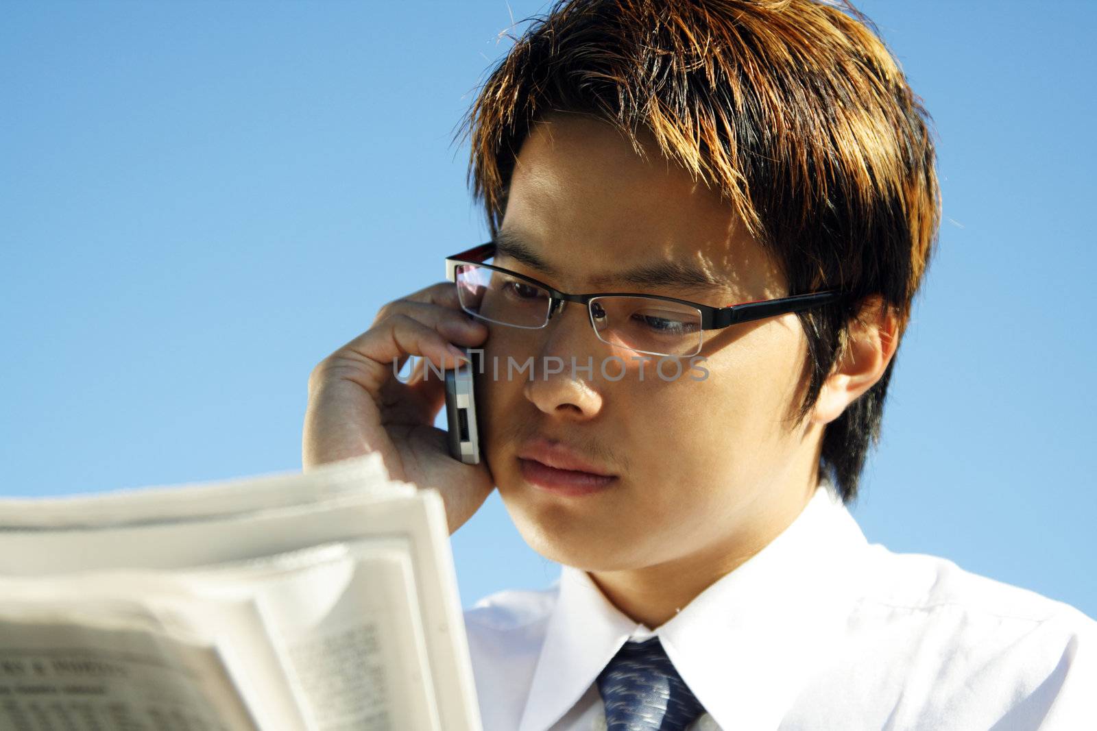 Businessman reading financial newspaper while making a phone call