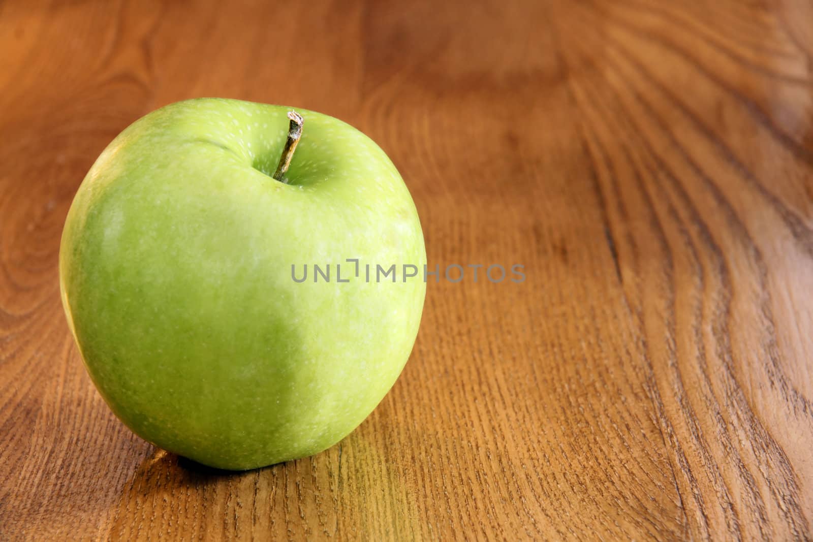 Healthy food: vibrant green granny smith apple on wooden kitchen table with copy space.