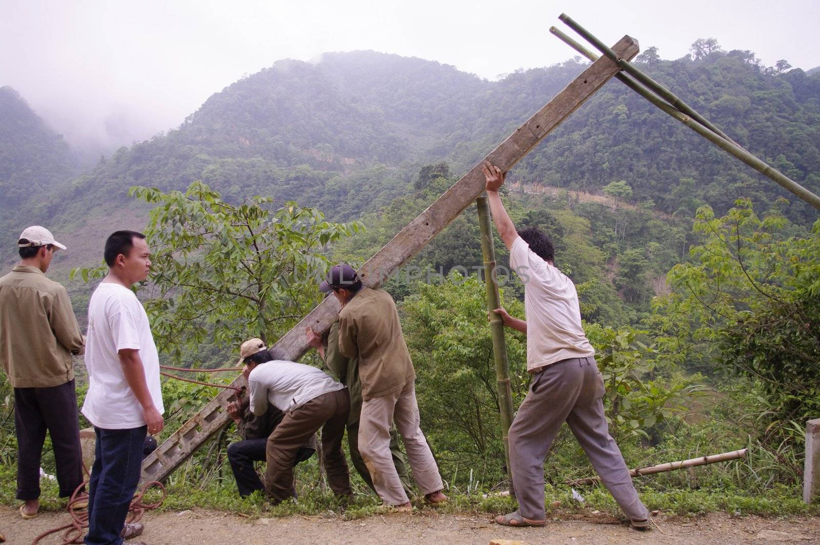 At the roadside stand men of concrete poles for laying electrical and telephone line. Nine men are needed for this dangerous operation. As the hole is in the slope of the precipice, at any time the post can slide carrying men with him. Men are usually held, no safety shoes, but flip-flops