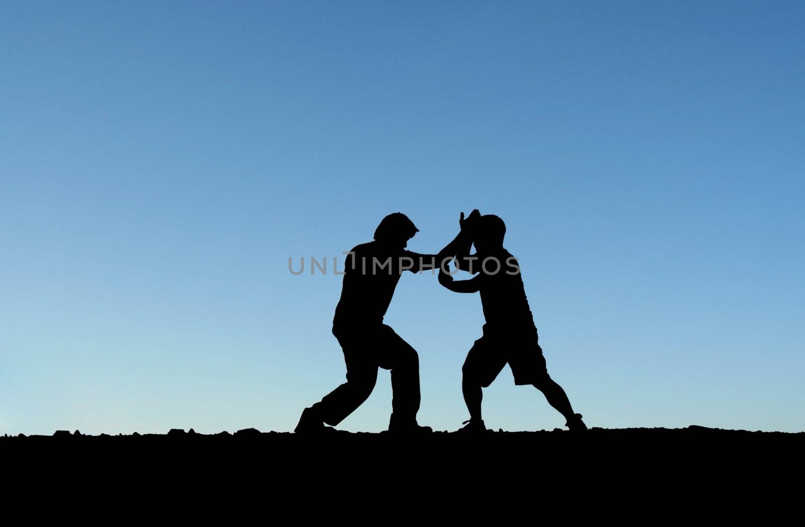 Two men practicing martial arts on top of a mountain (in silhouette)