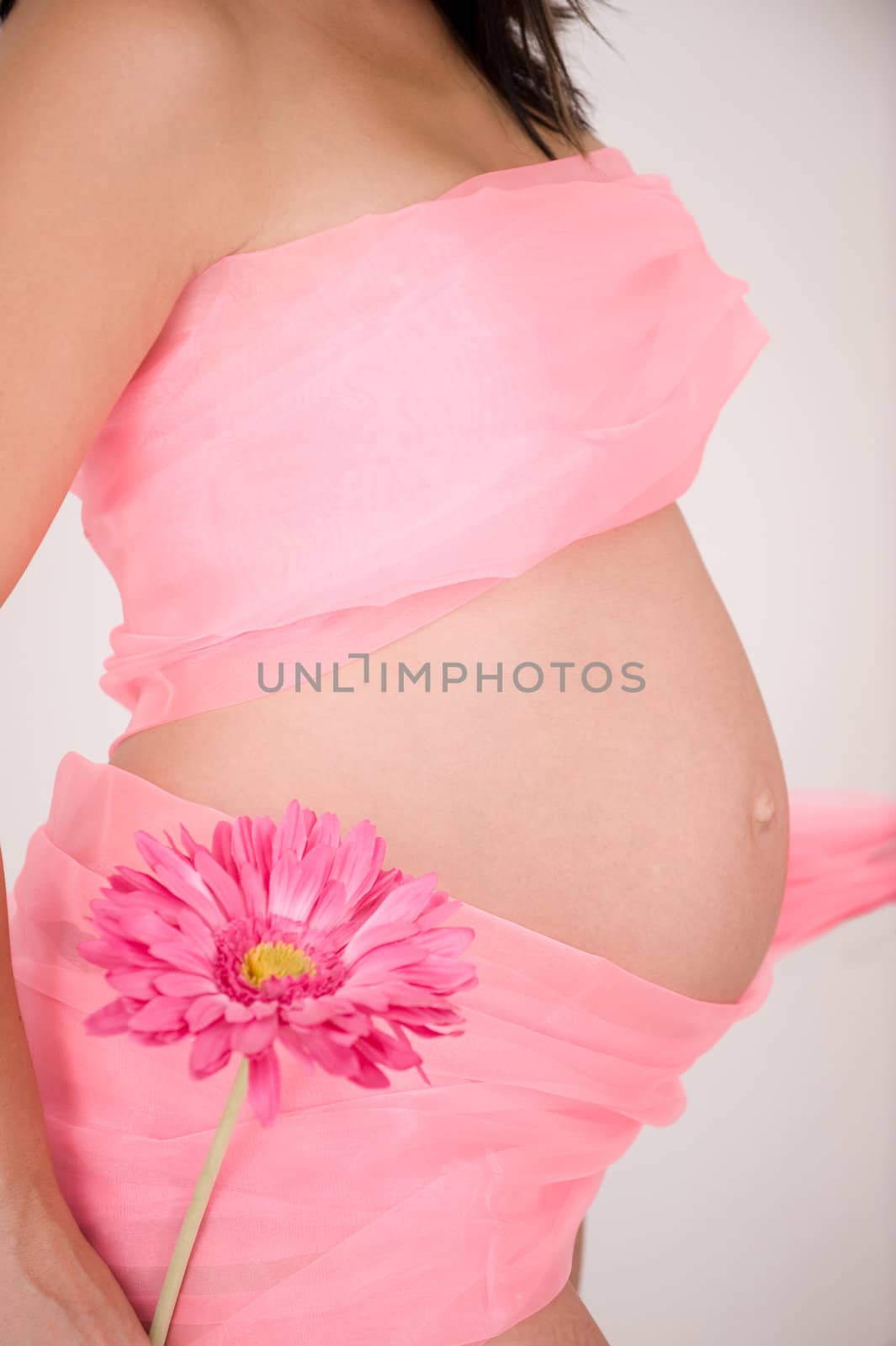 Pregnant young woman in pink showing belly and holding pink flower, sideview