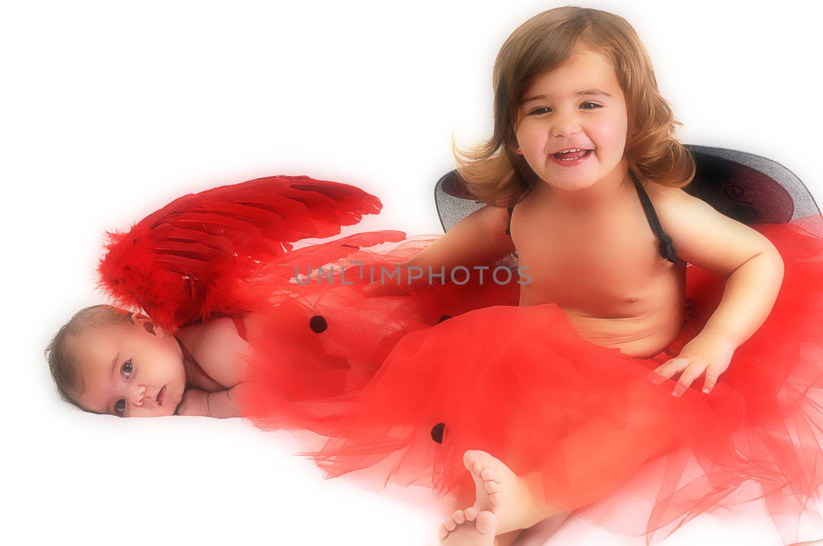 two sisters playing and smiling in studio wearing red angle wings