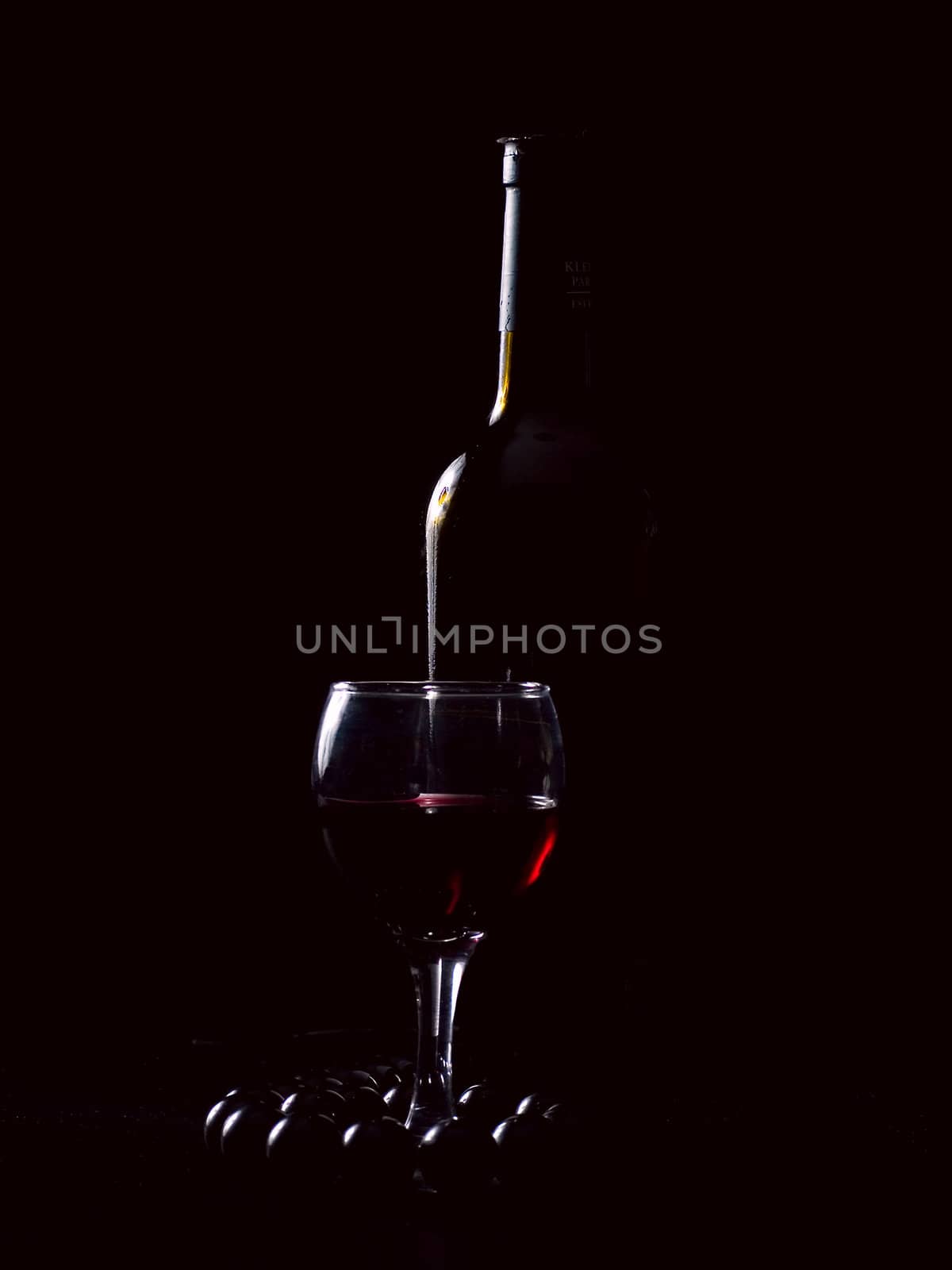 bottle, wineglass, beads on a black background. Studio light.Low key