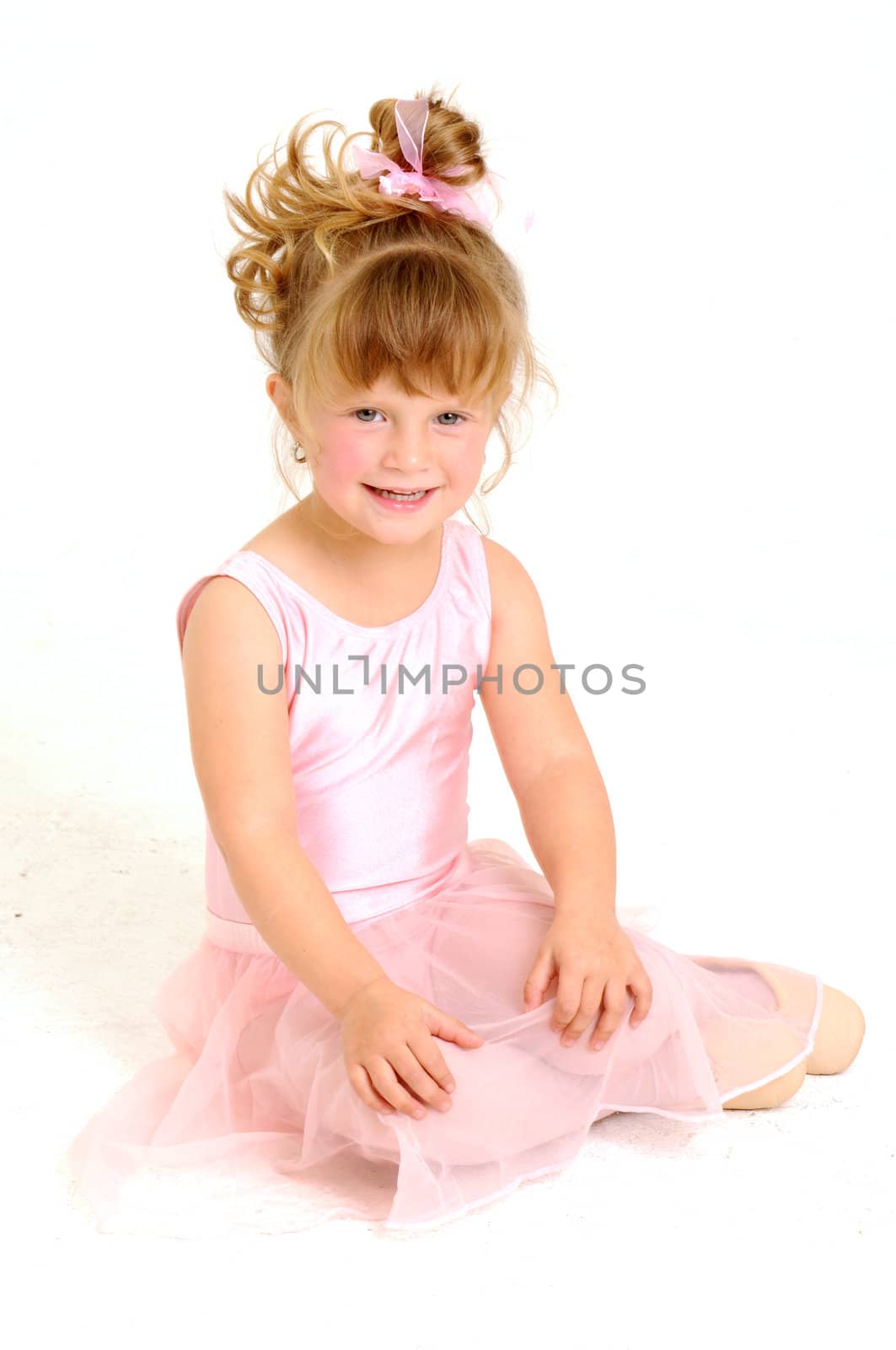 Little smiley girl wearing a pink ballet outfit is sitting on the floor