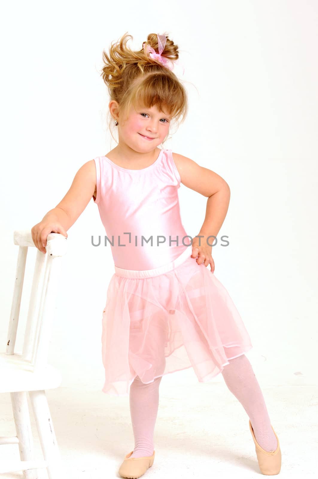 Little smiley girl wearing a pink ballet outfit is dancing holding her dress