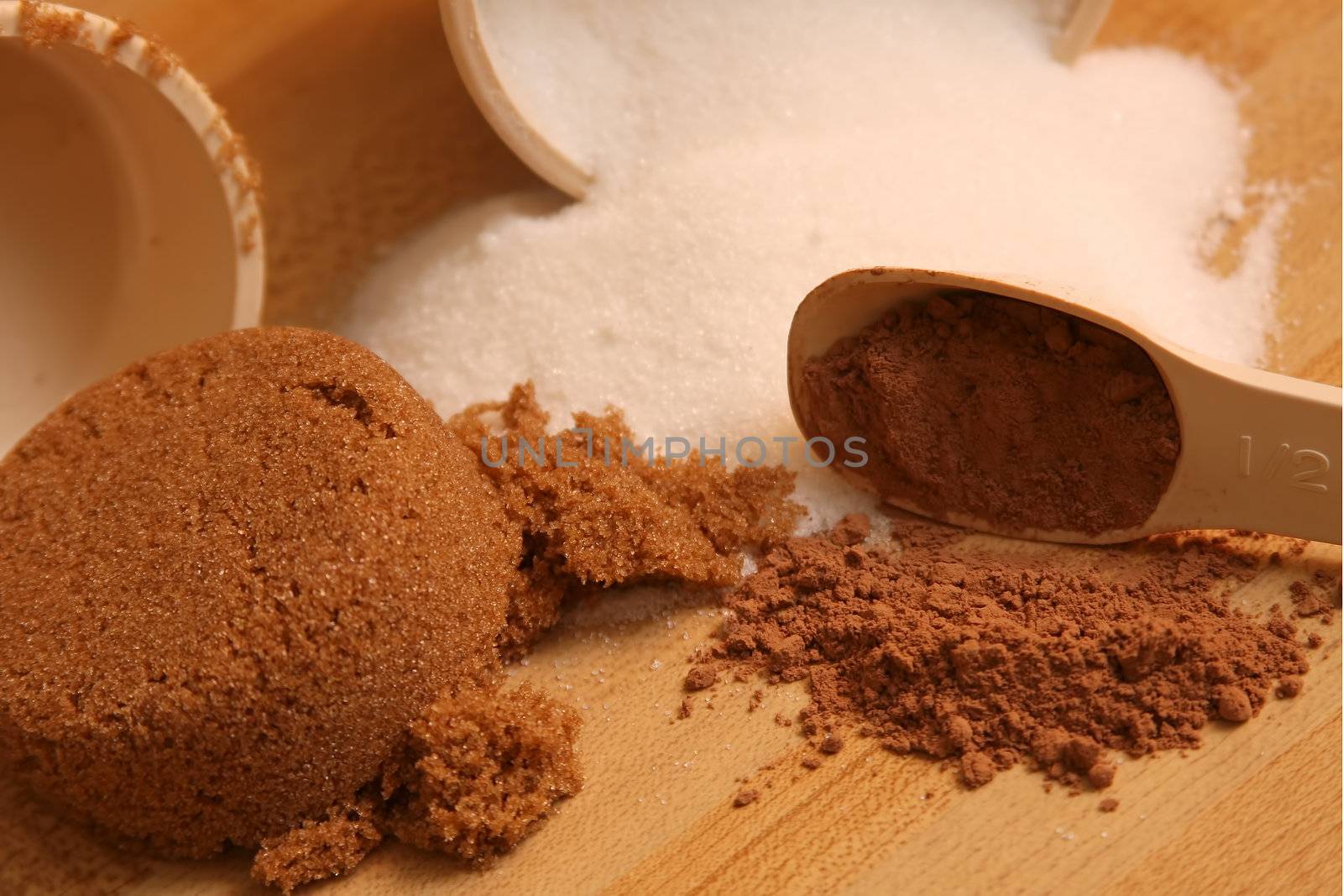 Brown and white sugar with cocoa in measuring cups and spoon.