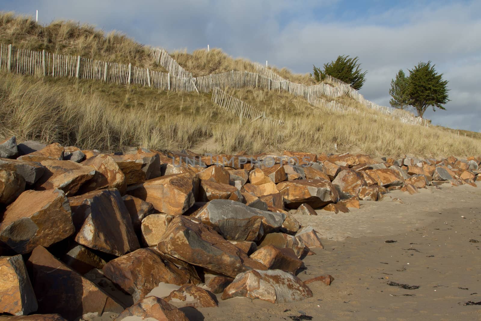 Rocks line the foot of a sand dune with criss-crossed wooden fences giving support to the mohair covered  sand dune.