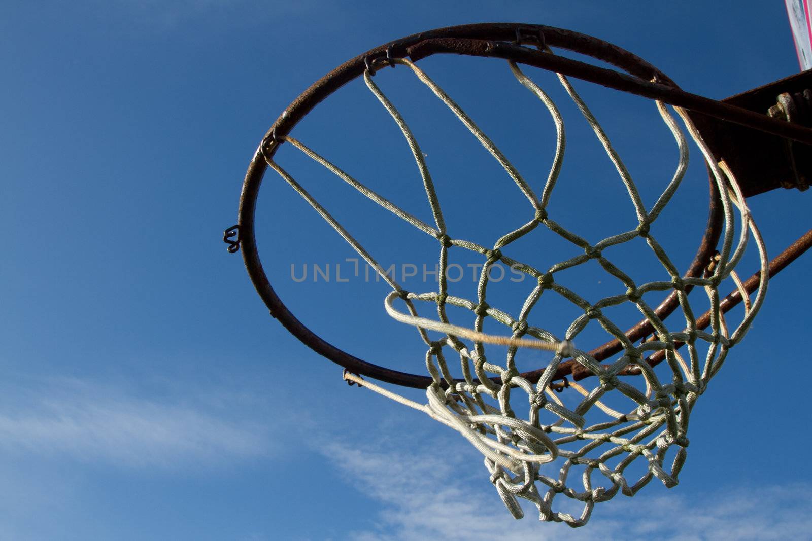 Basketball hoop, rusty ring and broken rope netting set against a blue sky.