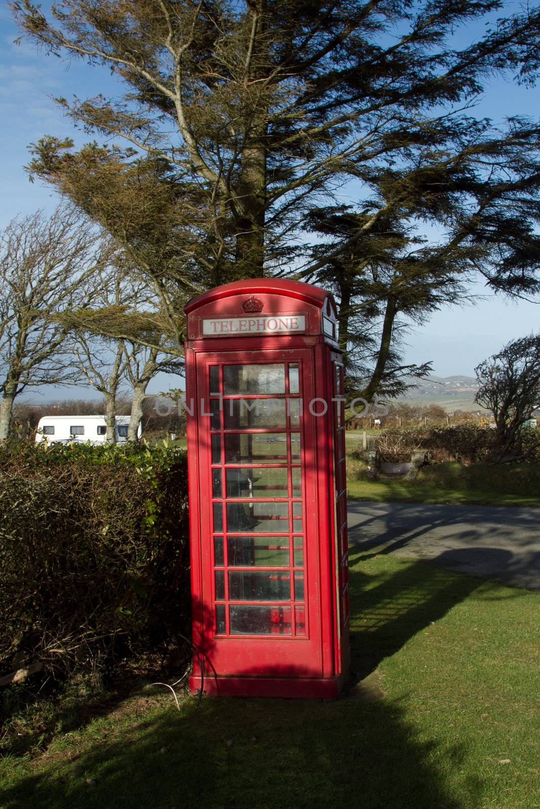 Vintage British red telephone box set under a shady tree on green grass.