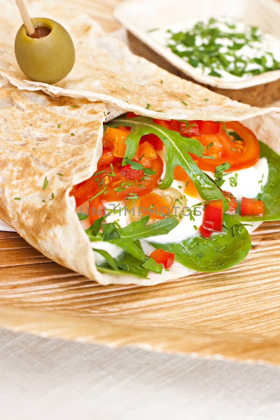 wheat wrap with olive filled with tomato, mozarello, bell pepper and salad. Some dip.
