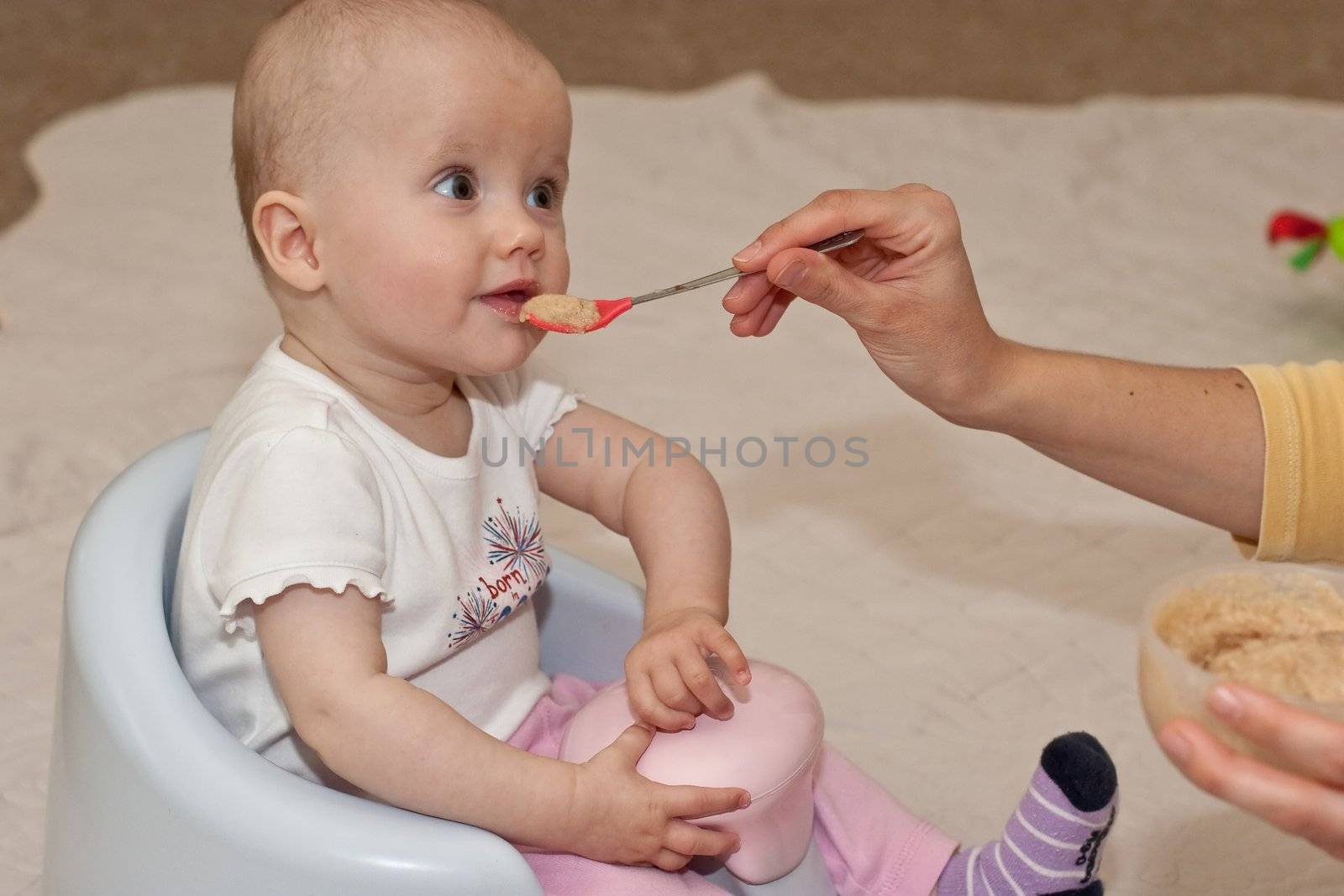 Mother is feeding little caucasian girl with oatmeal cereal.