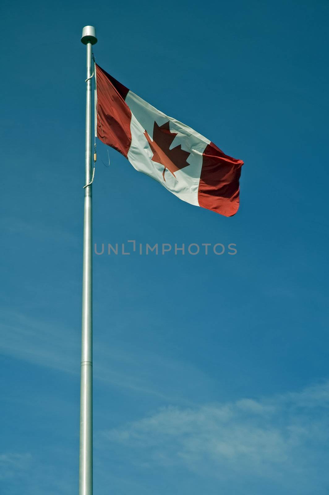 waving canadian flag on steel post, blue almost cloudless sky