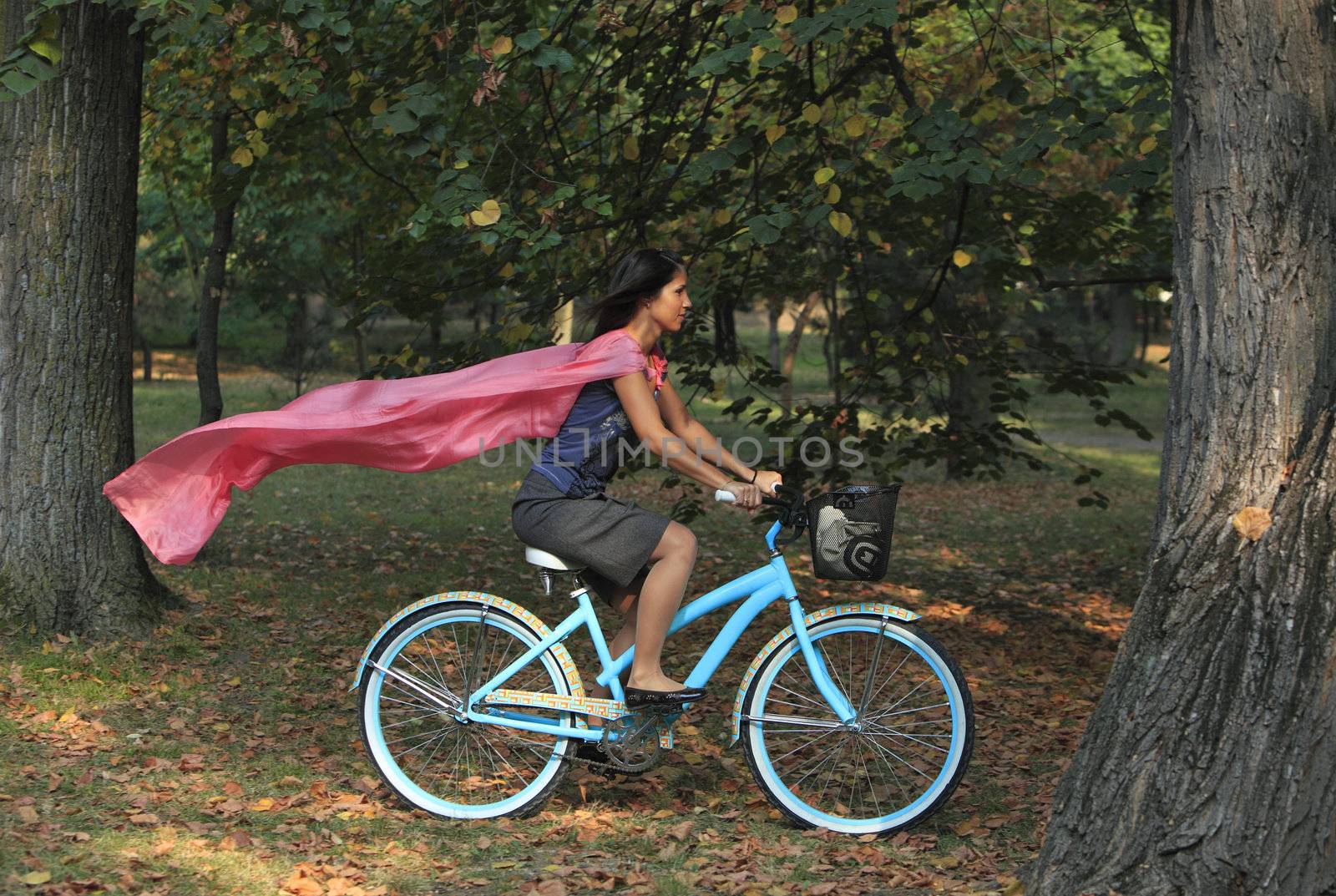 Image of a happy young woman with a pink scarf riding a bicycle in an early autumn park.