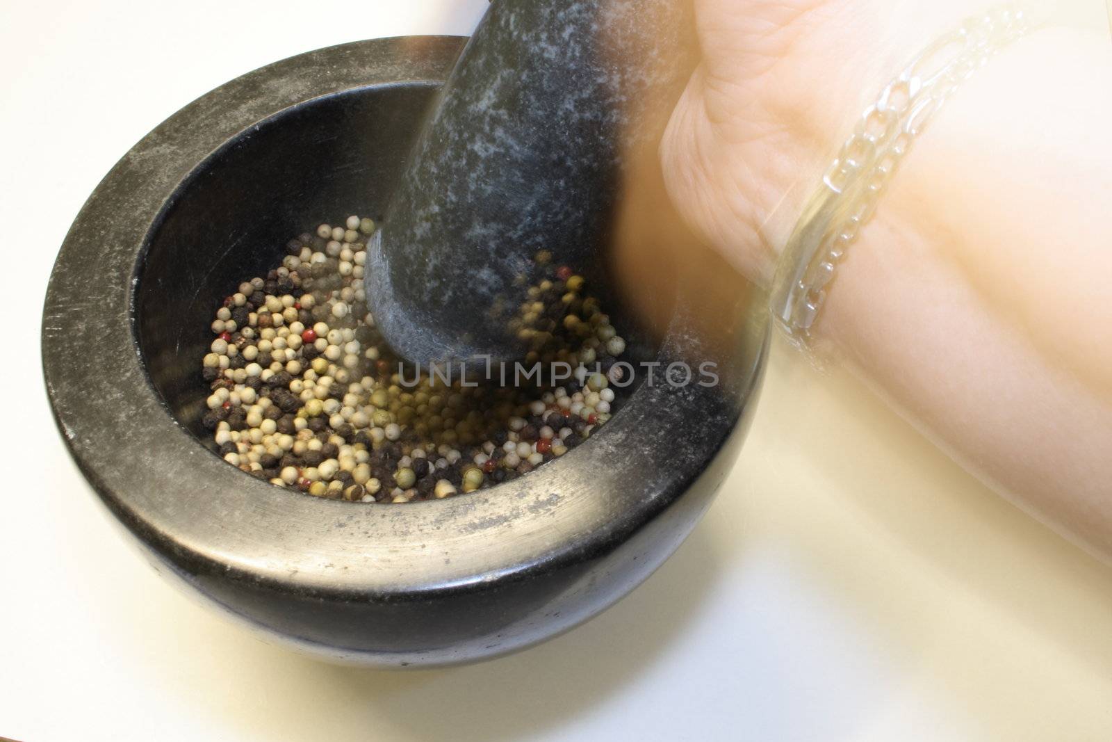 grinding peppercorns in a black granite pestle and mortar bowl showing the movement of the hand as it grinds the corns