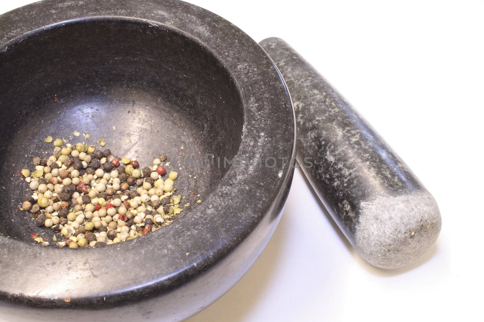 ground peppercorns in a black granite pestle and mortar bowl isolated over a white background