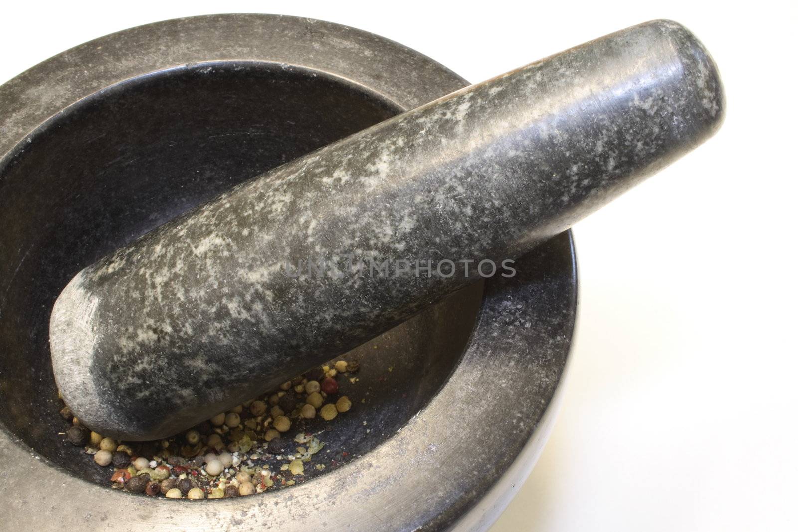 grinding pepper corns in a black granite pestle and mortar bowl isolated over a white background