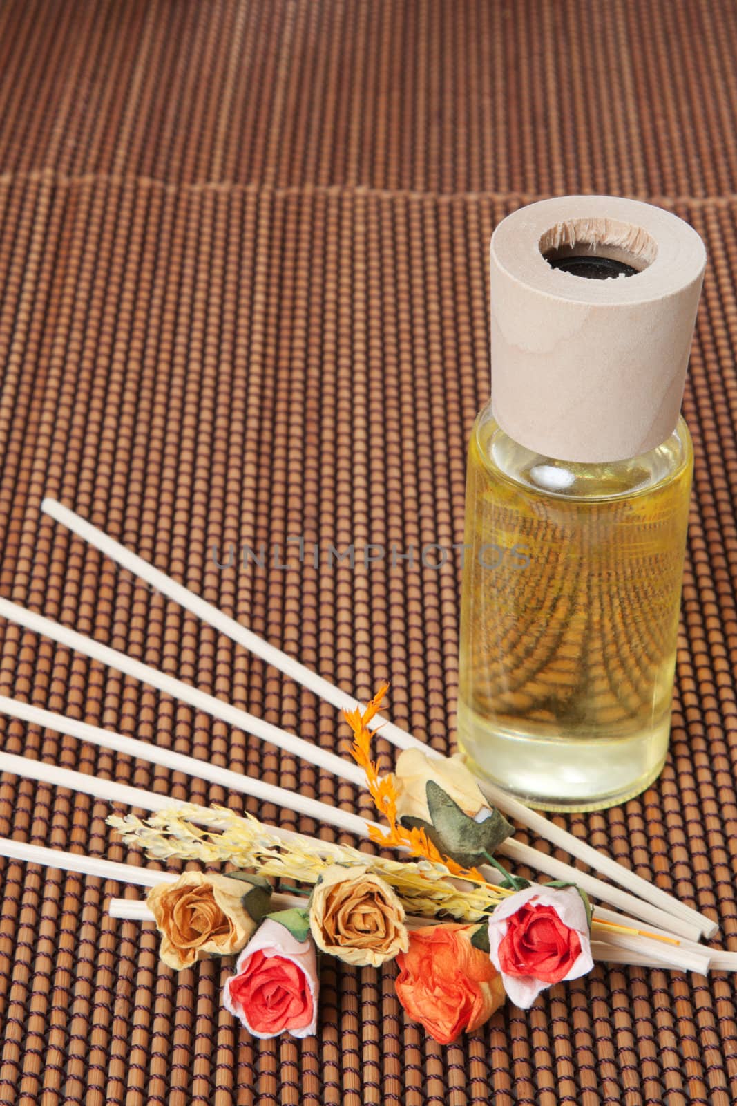 Glass bottle with yellow oil and small flowers lay on brown mat