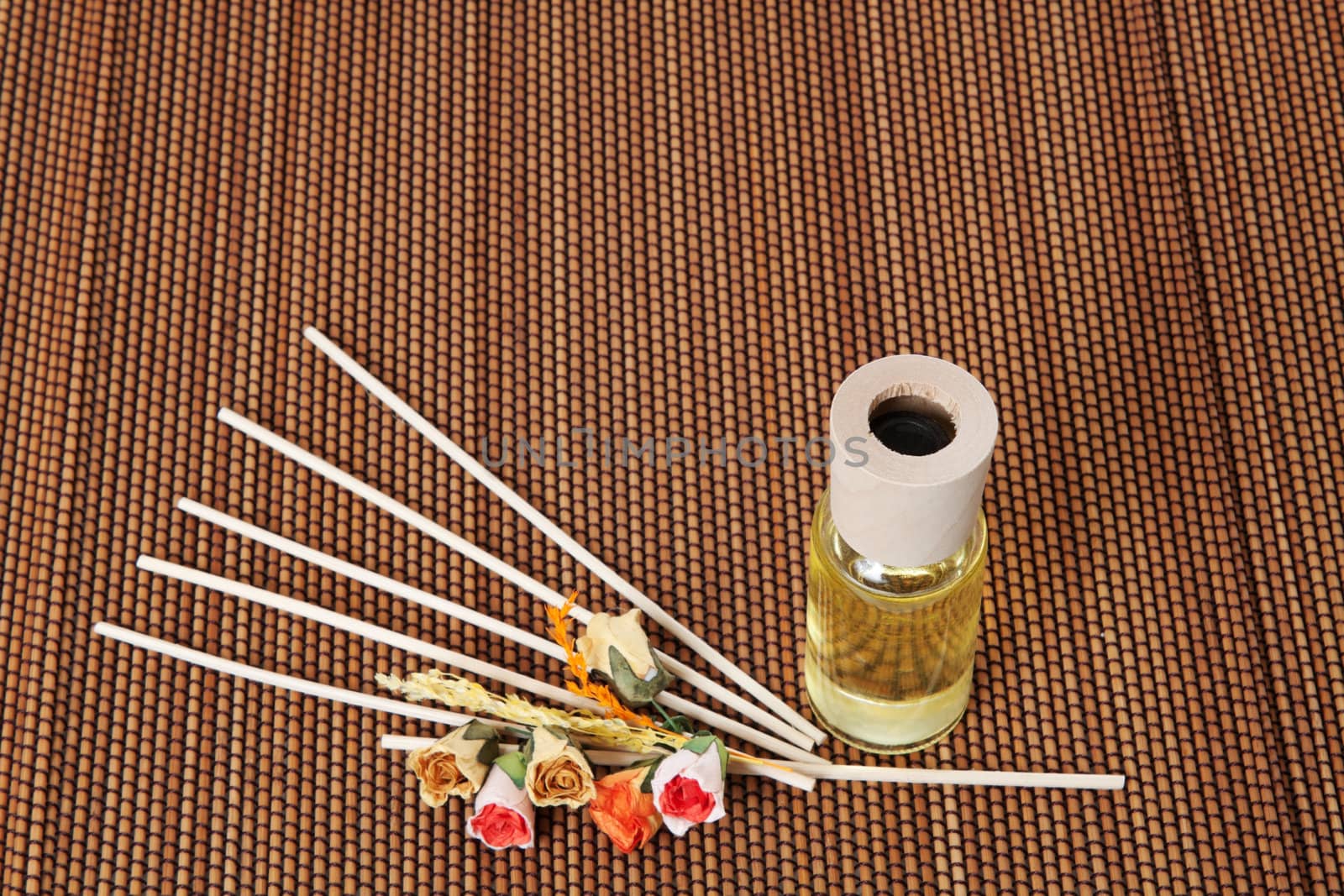 Glass bottle with yellow oil and small flowers lay on brown mat