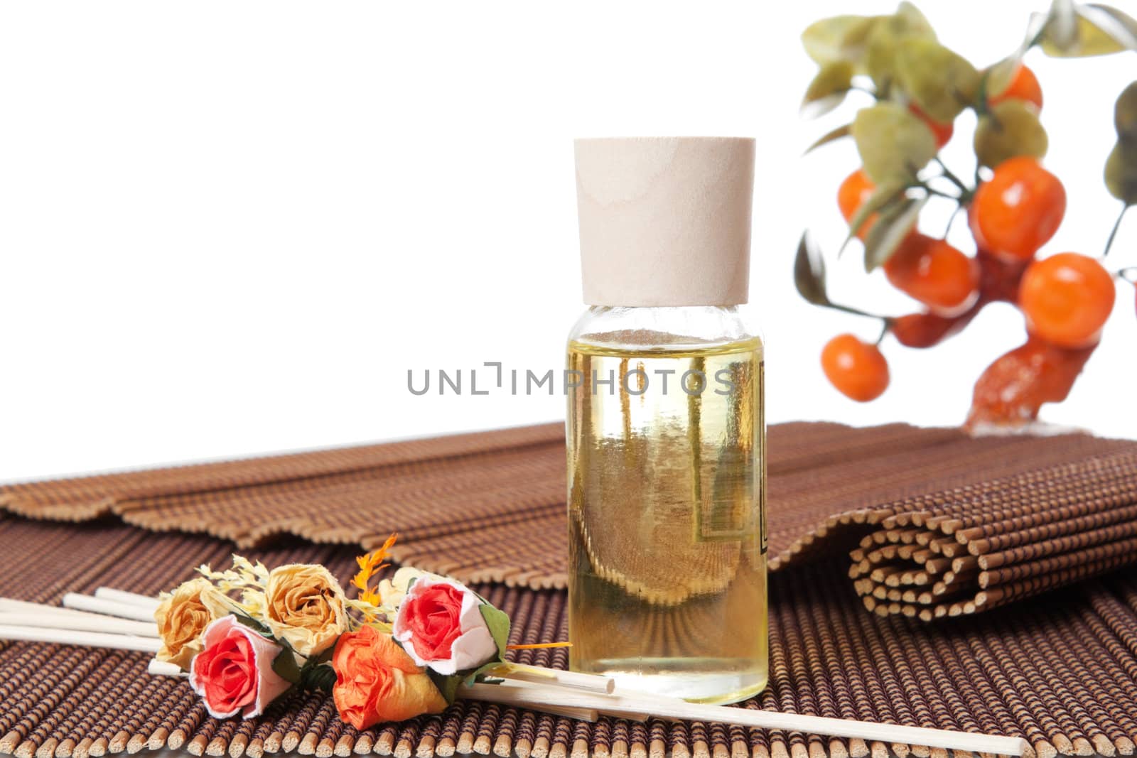 Glass bottle with yellow oil and small flowers lay on brown mat. Stone trees at the background