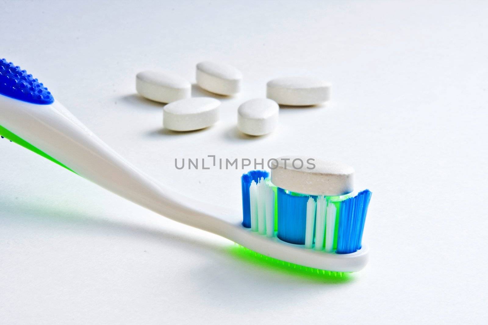 Calcium tablet resting on toothbrush bristles with other tablets in background