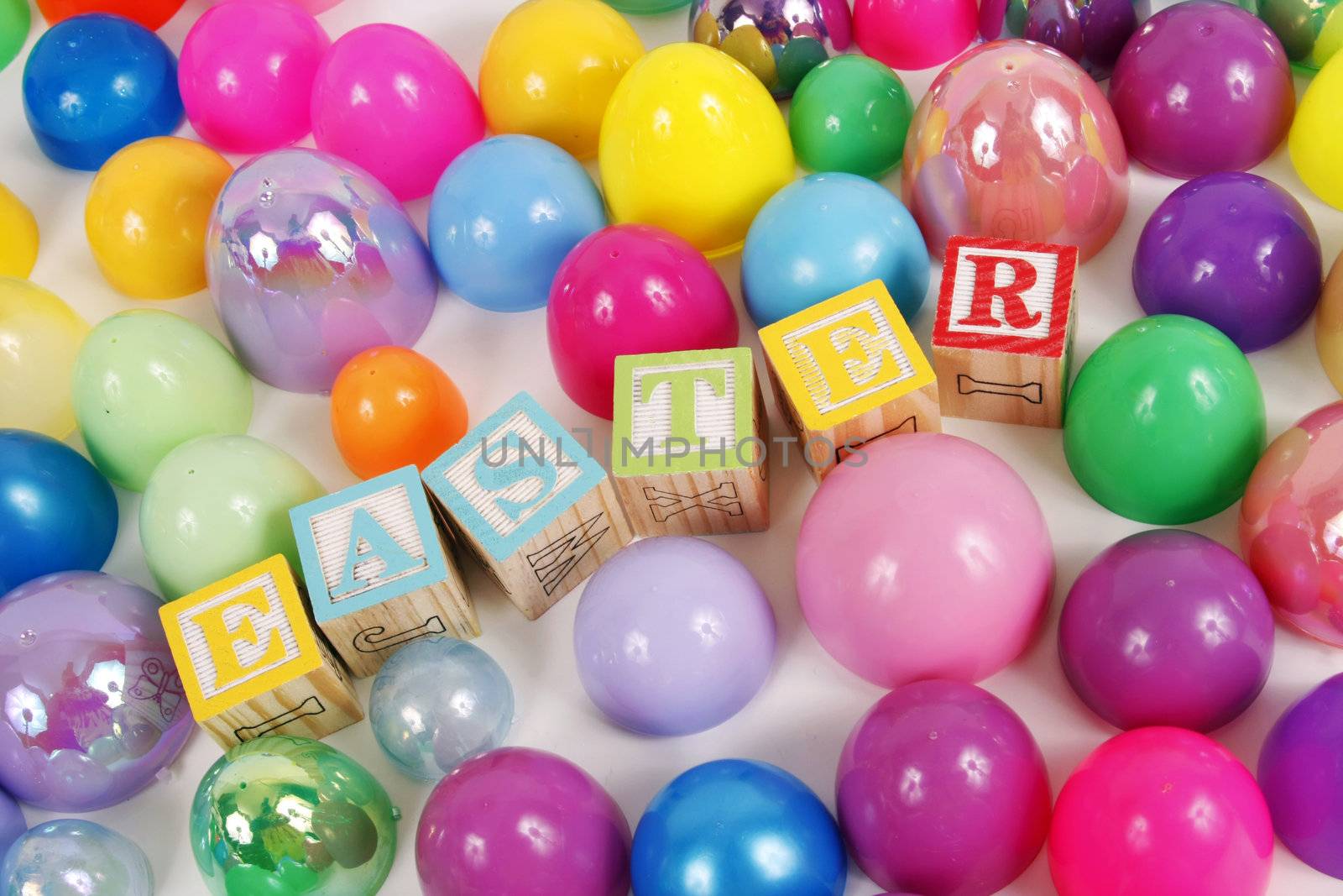 Childrens blocks spell Easter with colorful plastic eggs on a white background.
