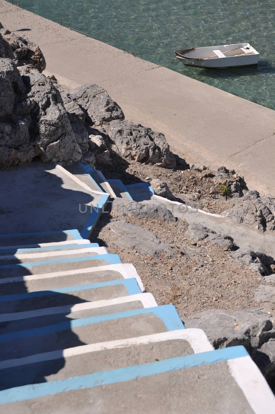 traditional white and blue stairway in a Pserimos greek island (focus on the boat)