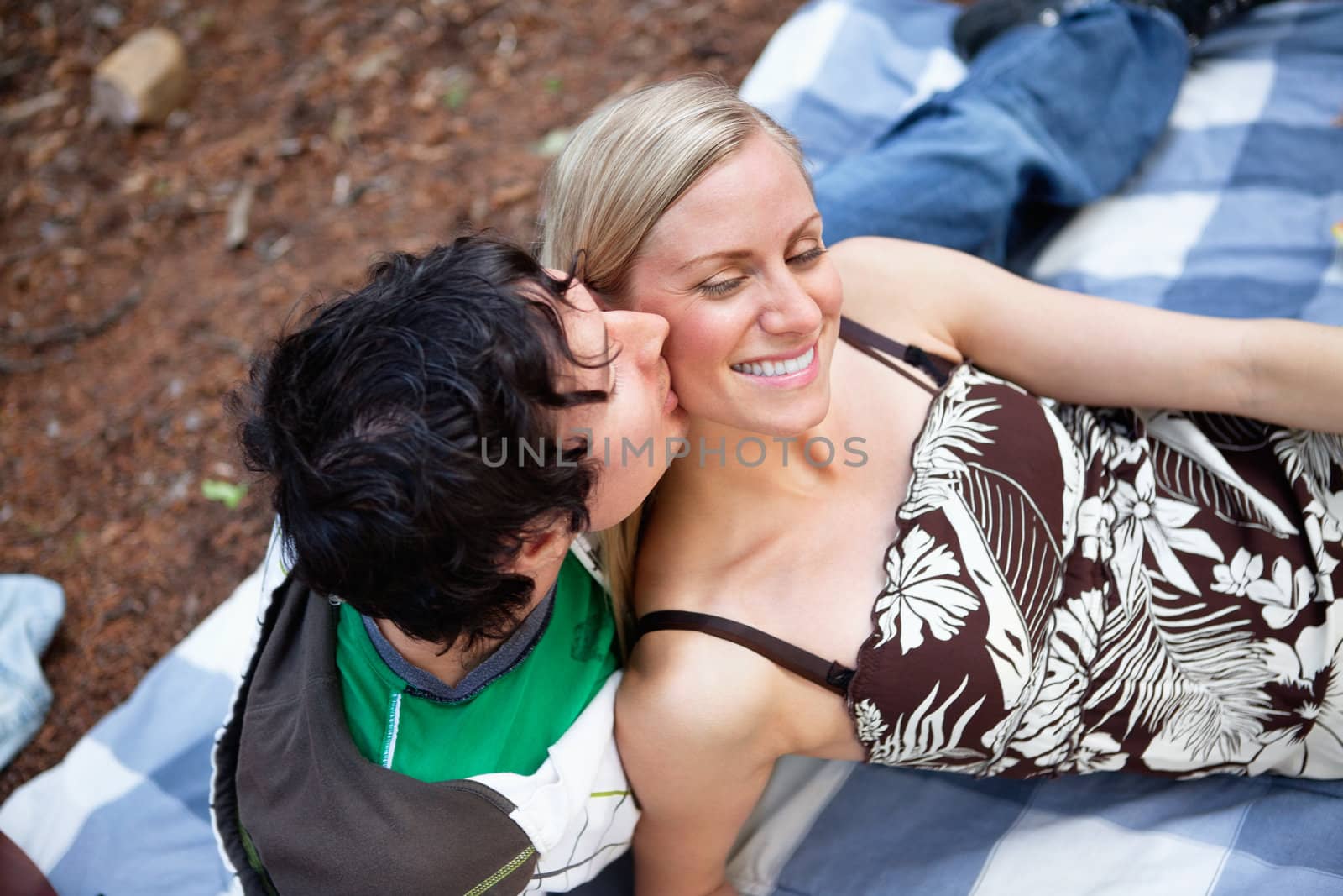 Top view of romantic young guy kissing happy female while on picnic