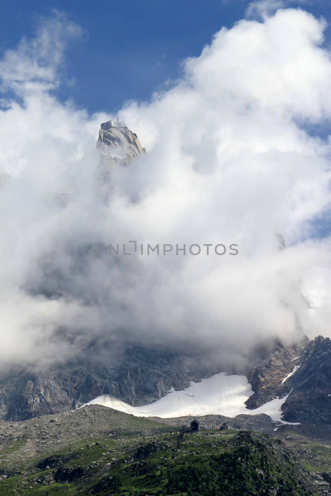View of Aiguille Du Midi surrounded by lots of clouds and deep blue sky from Chamonix, France