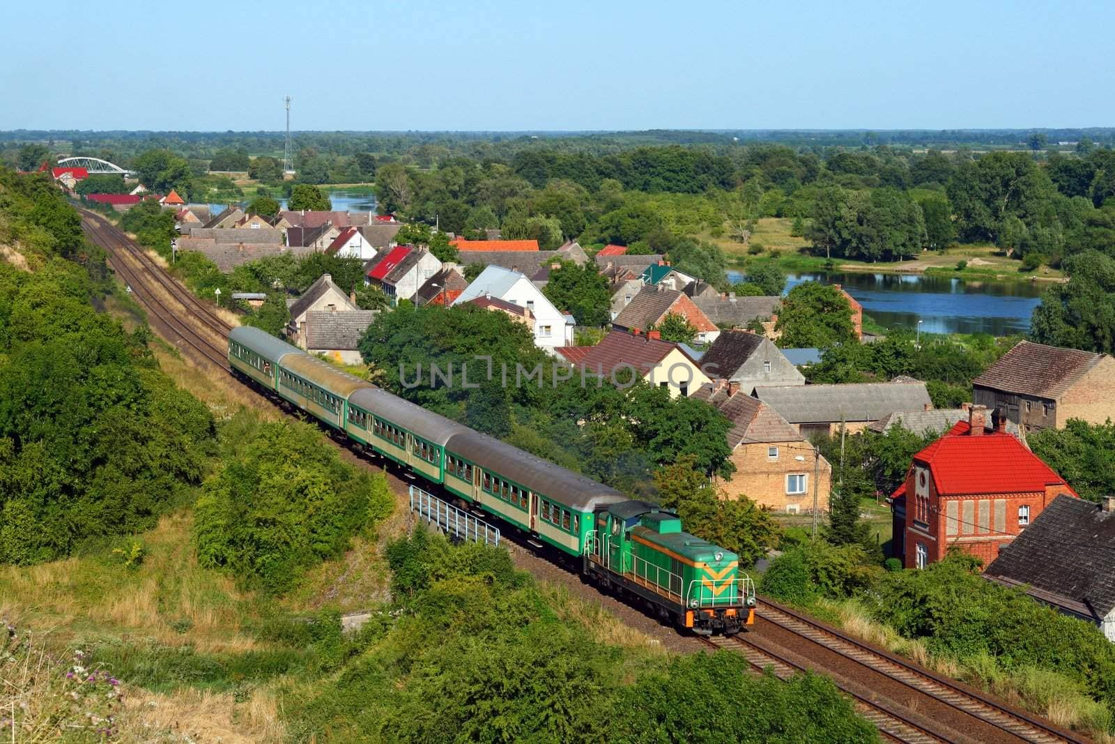 Passenger train passing the village with the river in background