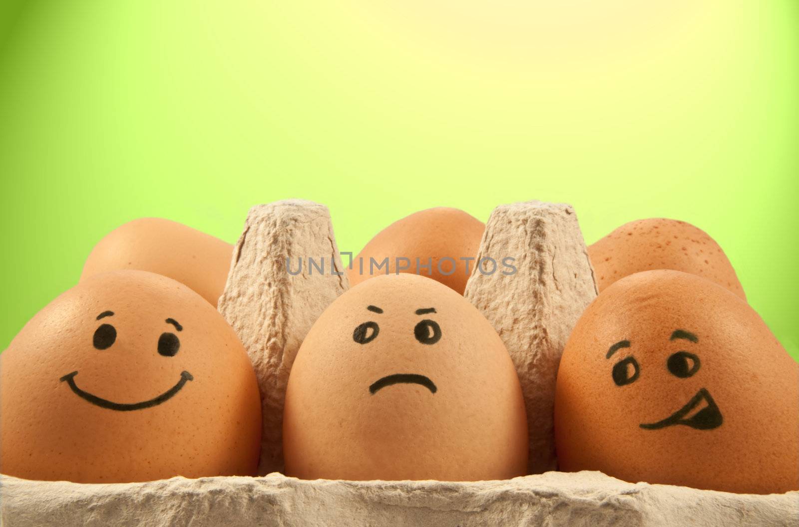 Close and low level of several brown eggs with painted faces against green and yellow light effect background