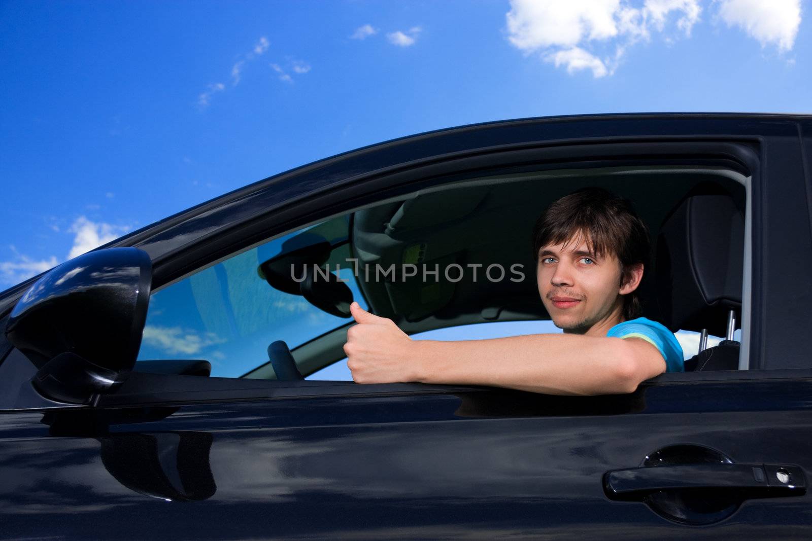 Successful young man sitting in own car against blue sky