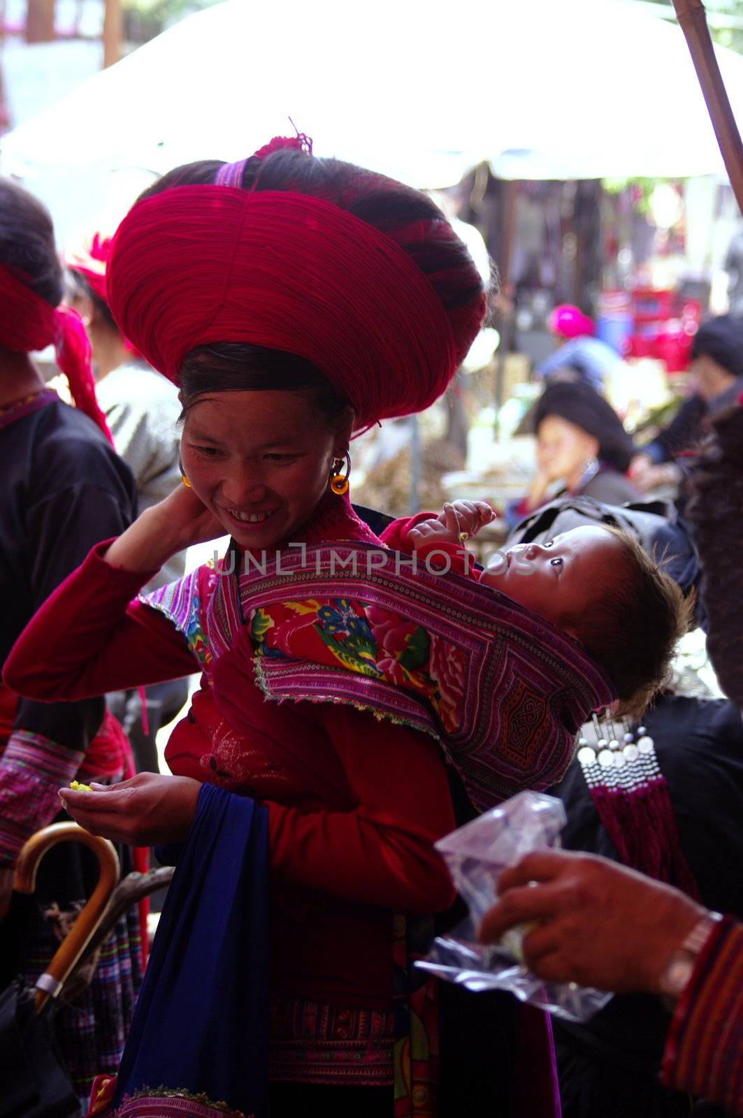 Young red Hmong woman with baby in the back . HE COME TO Sin Ho market. For the feast she make with red wool and her long hairs black.Hairstyle typical red Hmong in Lai Chau province