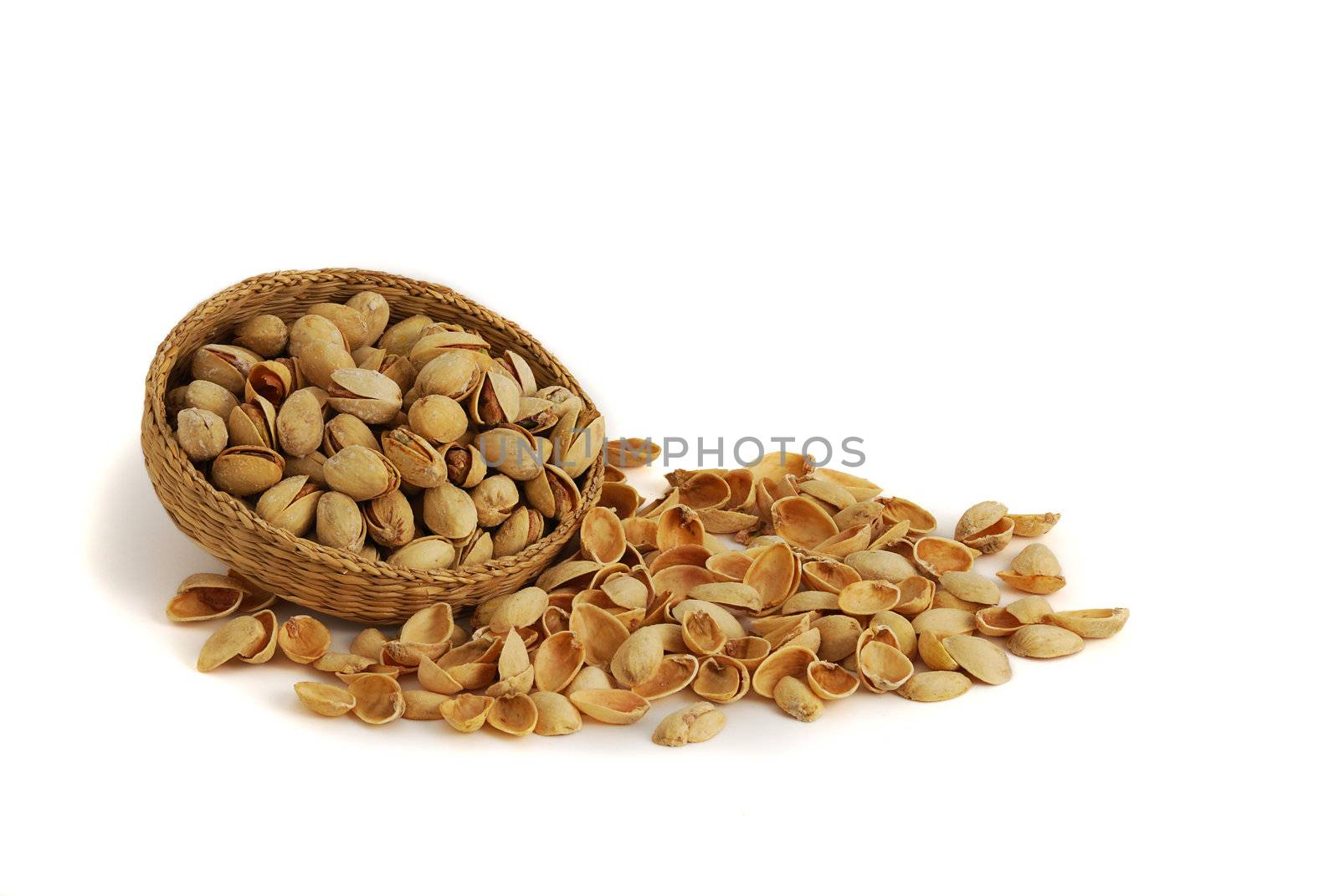 Pistachios in interwoven bowl with spilled nutshells on white background