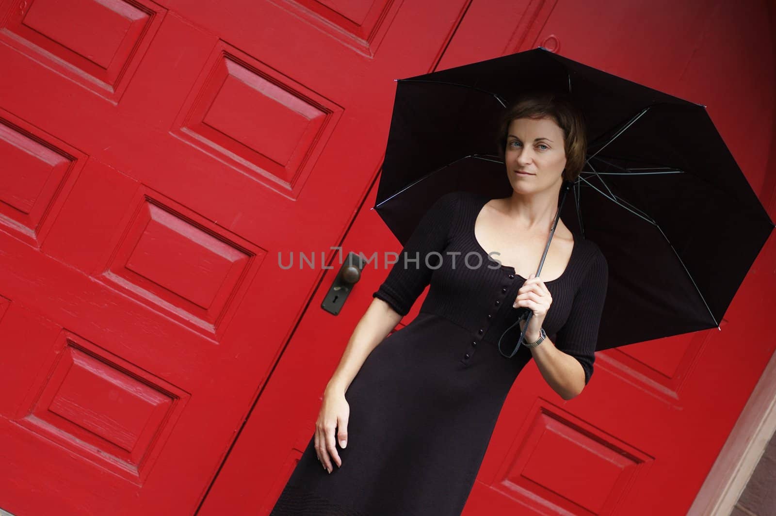 Woman with umbrella in front of red doors.