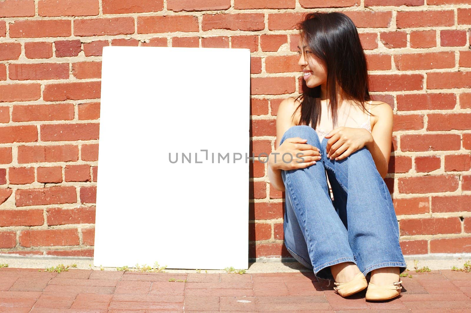 Fashionable girl with blank white poster against brick wall.