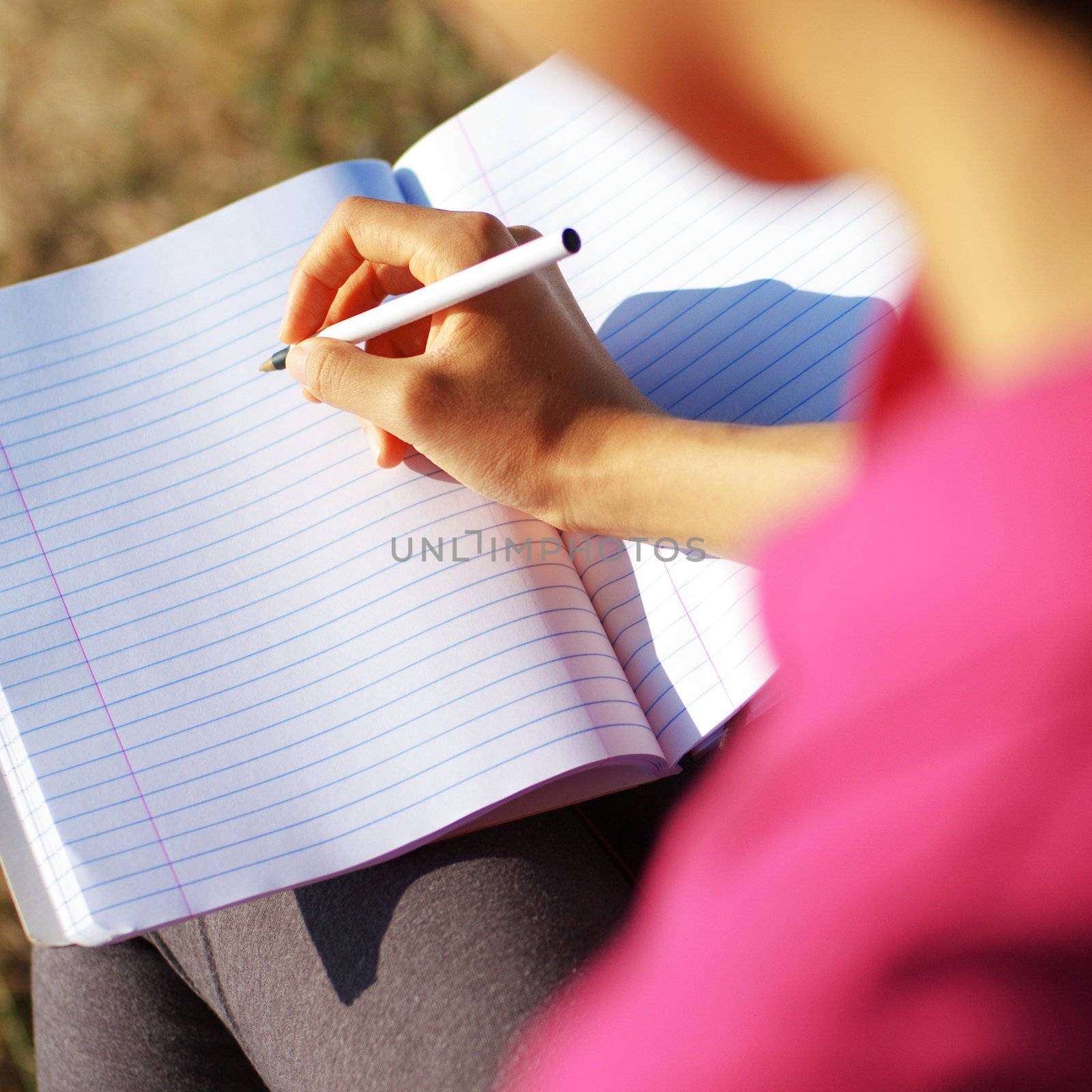 Girl writing in notebook in a field.