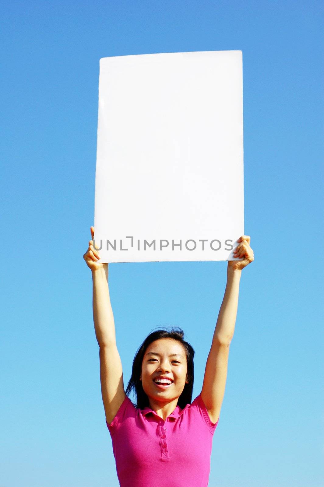 Girl holding blank sign in front of big blue sky.