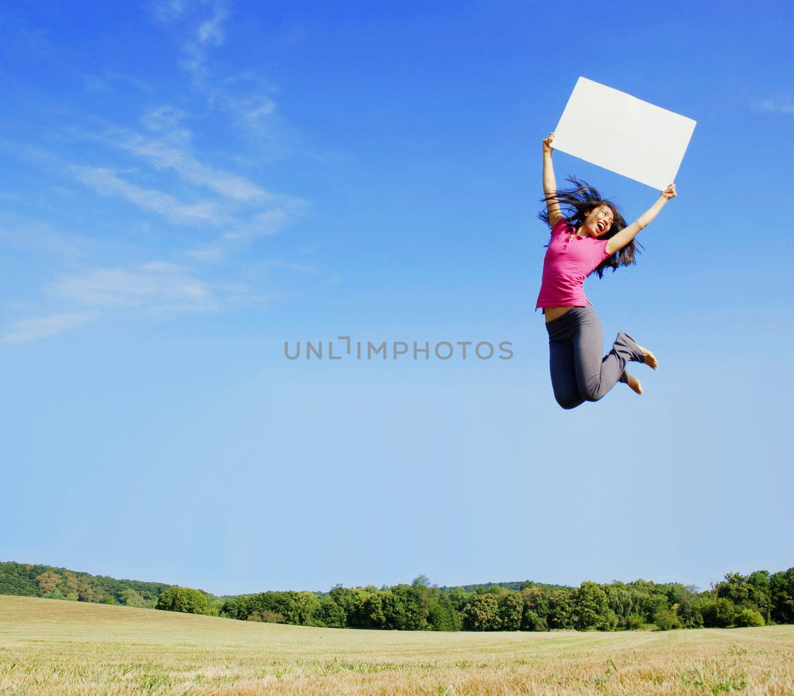 Girl jumping with a blank sign in a field.