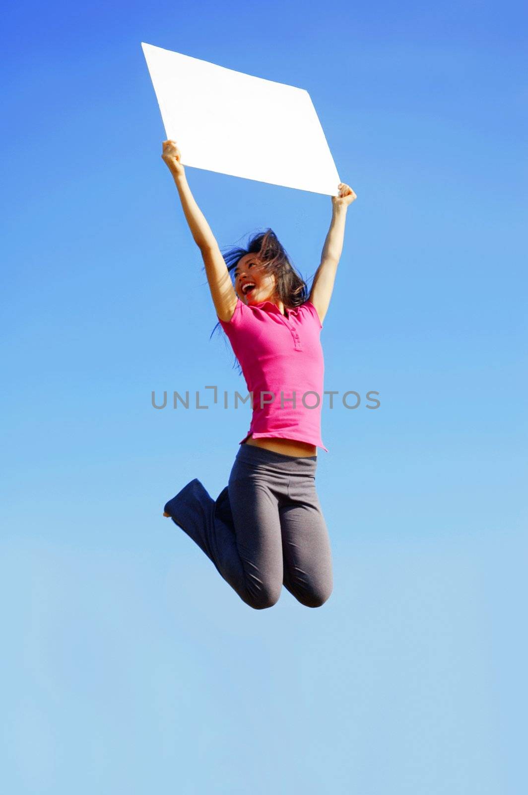 Girl jumping with sign in front of a big blue sky.