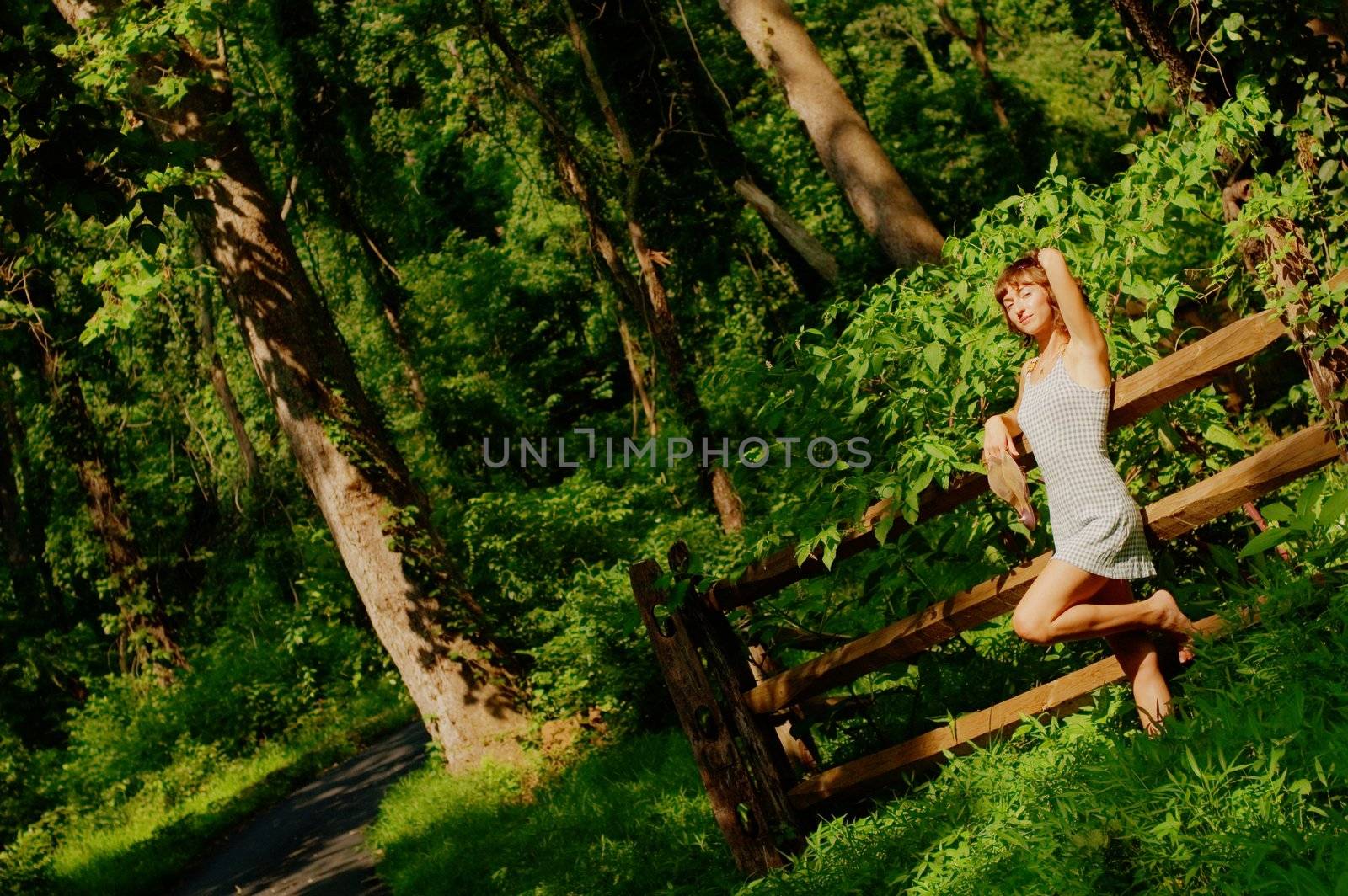 Pretty girl leaning against fence in woods.