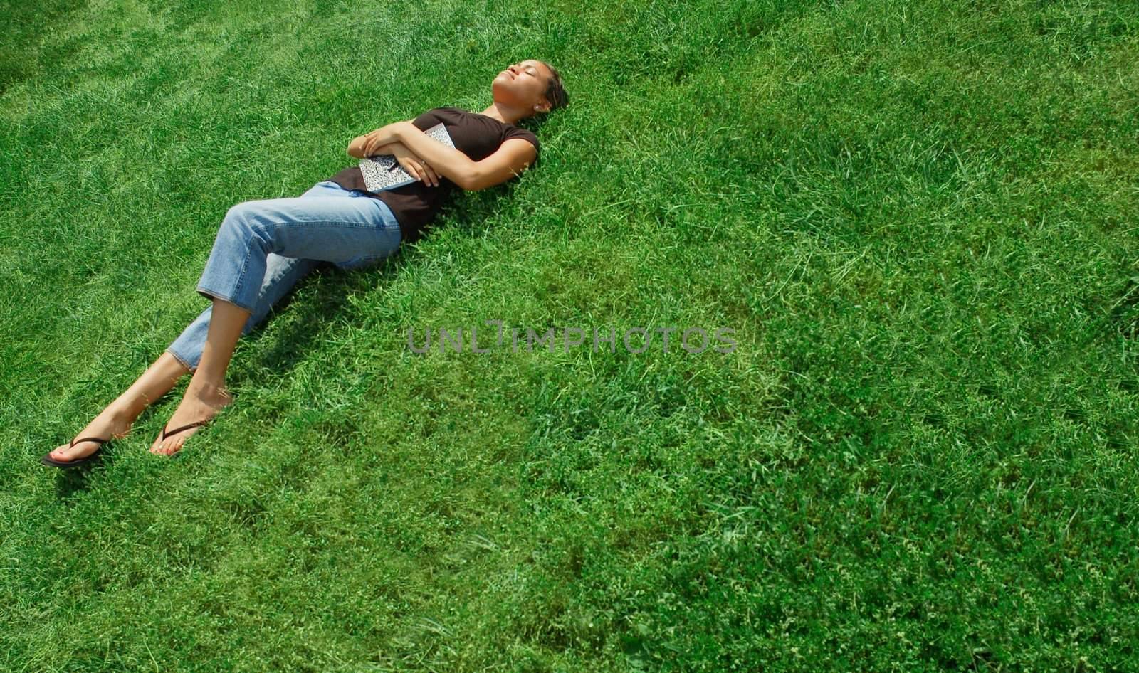 Beautiful young woman laying in green field with notebook.