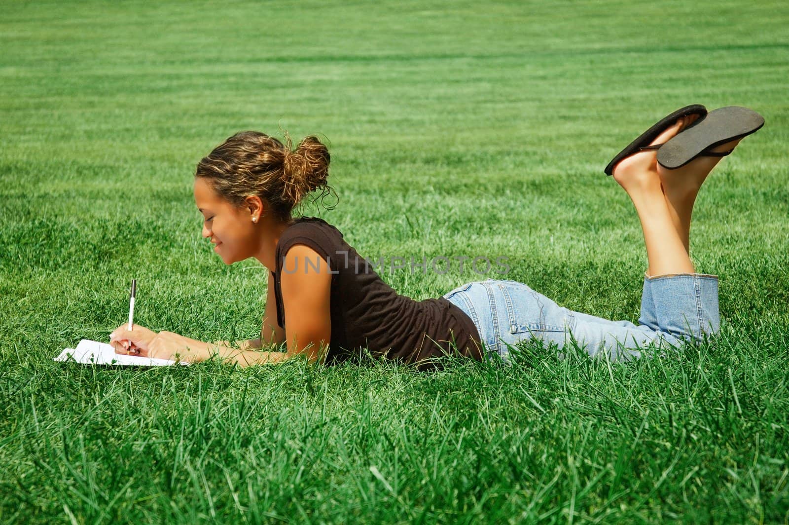 Beautiful young woman in green field with notebook.