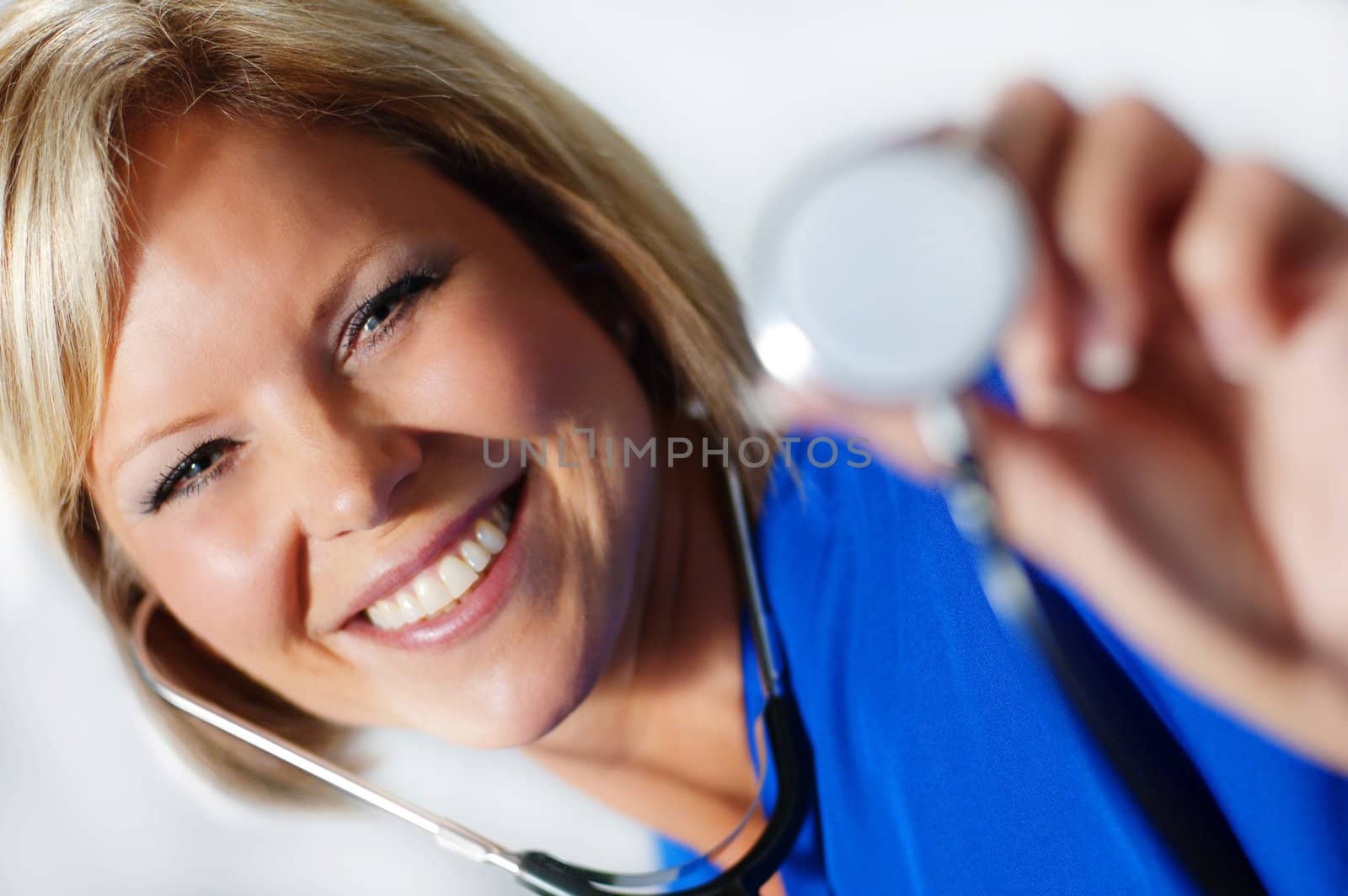 Mature nurse in scrubs holding up stethoscope.