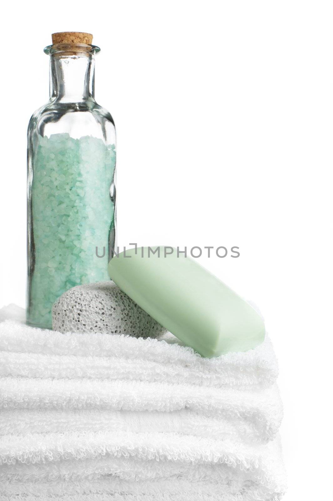 Bath salt, pumice stone, bar soap, and towels against white.