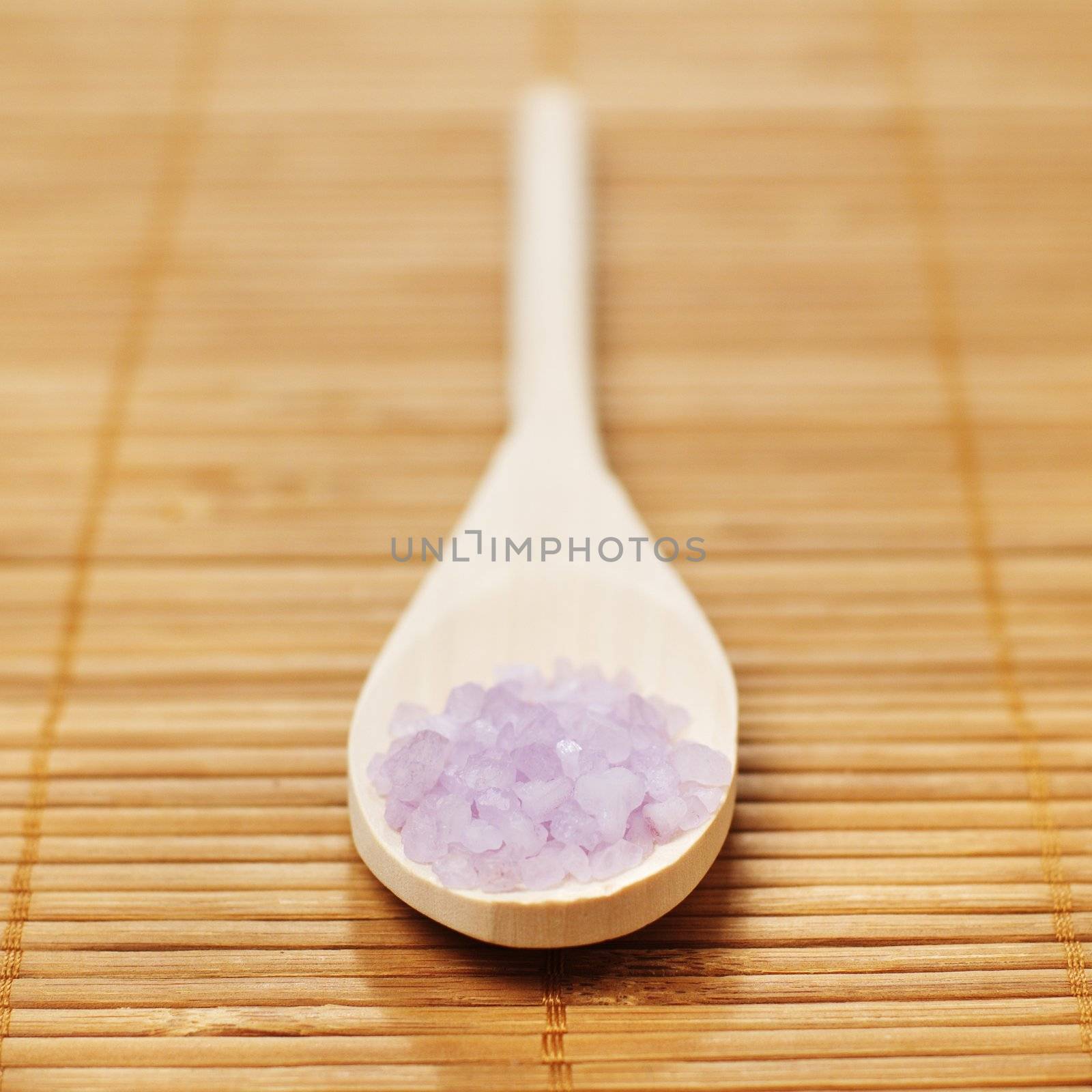 Bath salt and wooden spoon on display against bamboo mat.