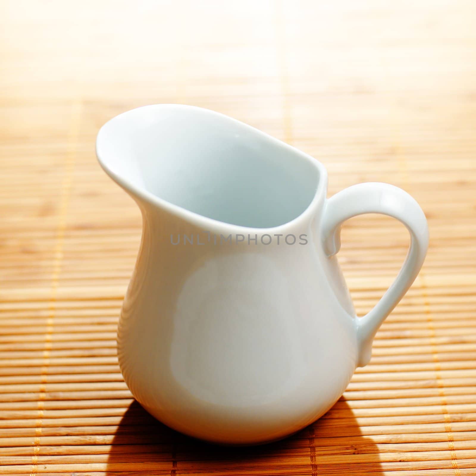 White pitcher on display against a bamboo mat.